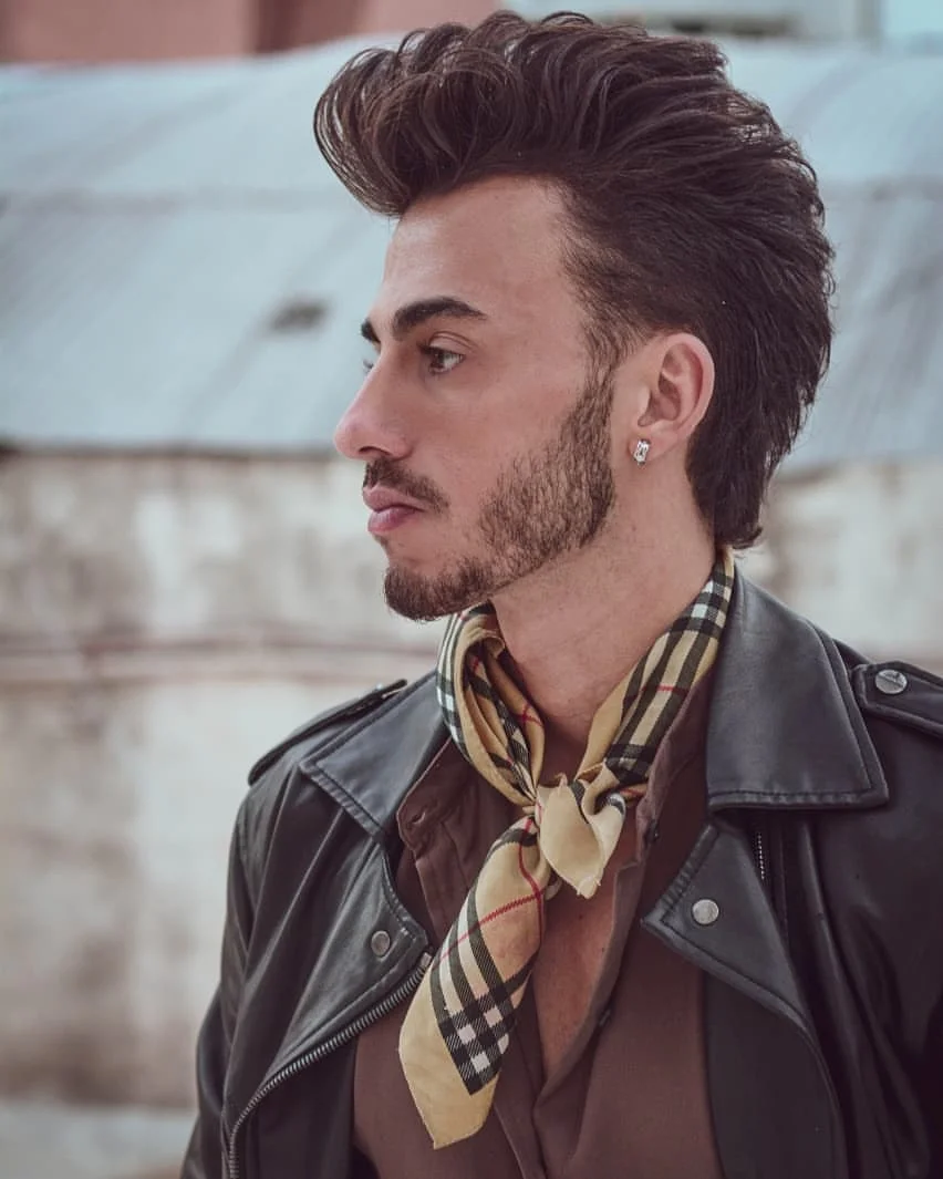 Pompadour alto con los laterales cerrados y la barba prolija.